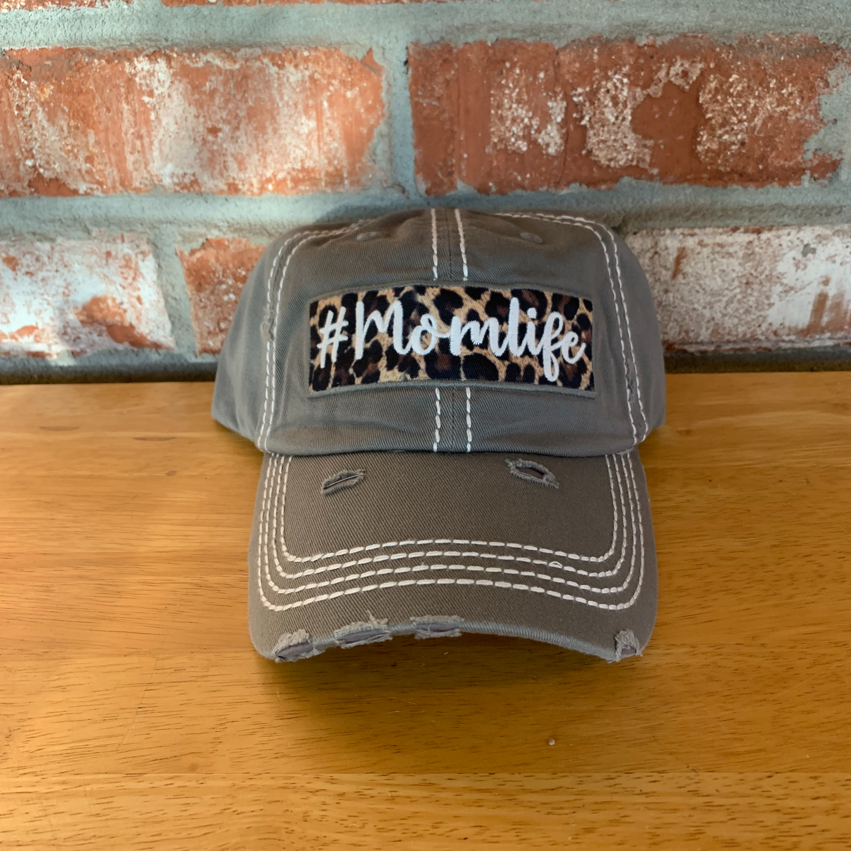 Gray distressed hat with a patch. Underneath the bill of the hat is also leopard print. 