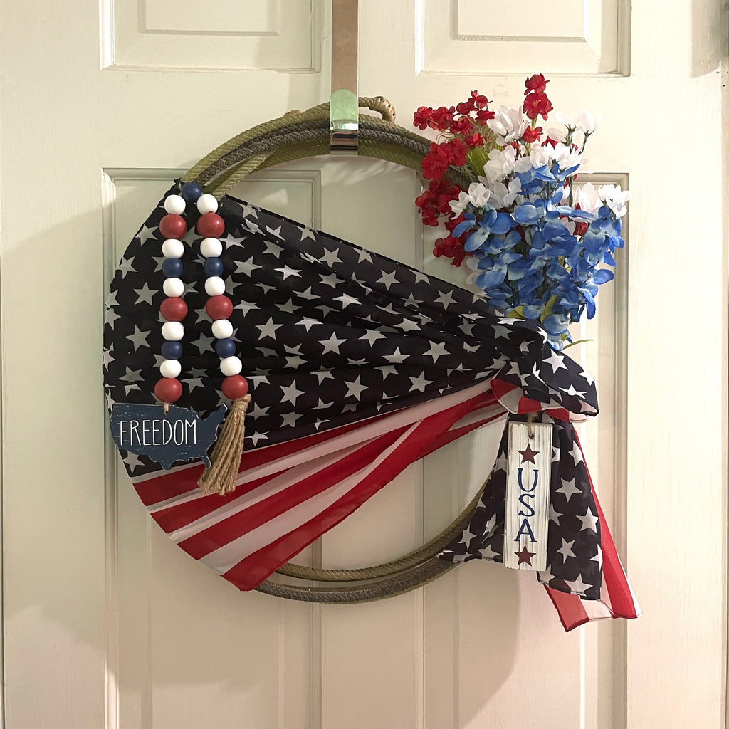 Handcrafted patriotic wreath on an upcycled lariat roping rope. Width: Approximately 19 inches. Florals and patriotic decorations.