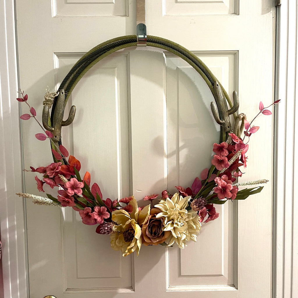 Handcrafted wreath on an upcycled lariat roping rope. Width: Approximately 21 inches. Florals and metal cactuses. 