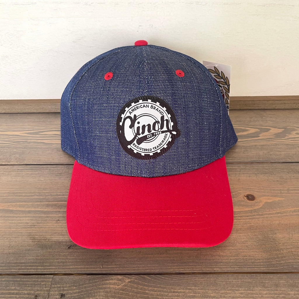 Cinch men's cap. Textured logo patch on the front. One size fits most. Adjustable snapback closure. Solid back with eyelets. Colorblock design. Denim/Red Contrast curved bill.