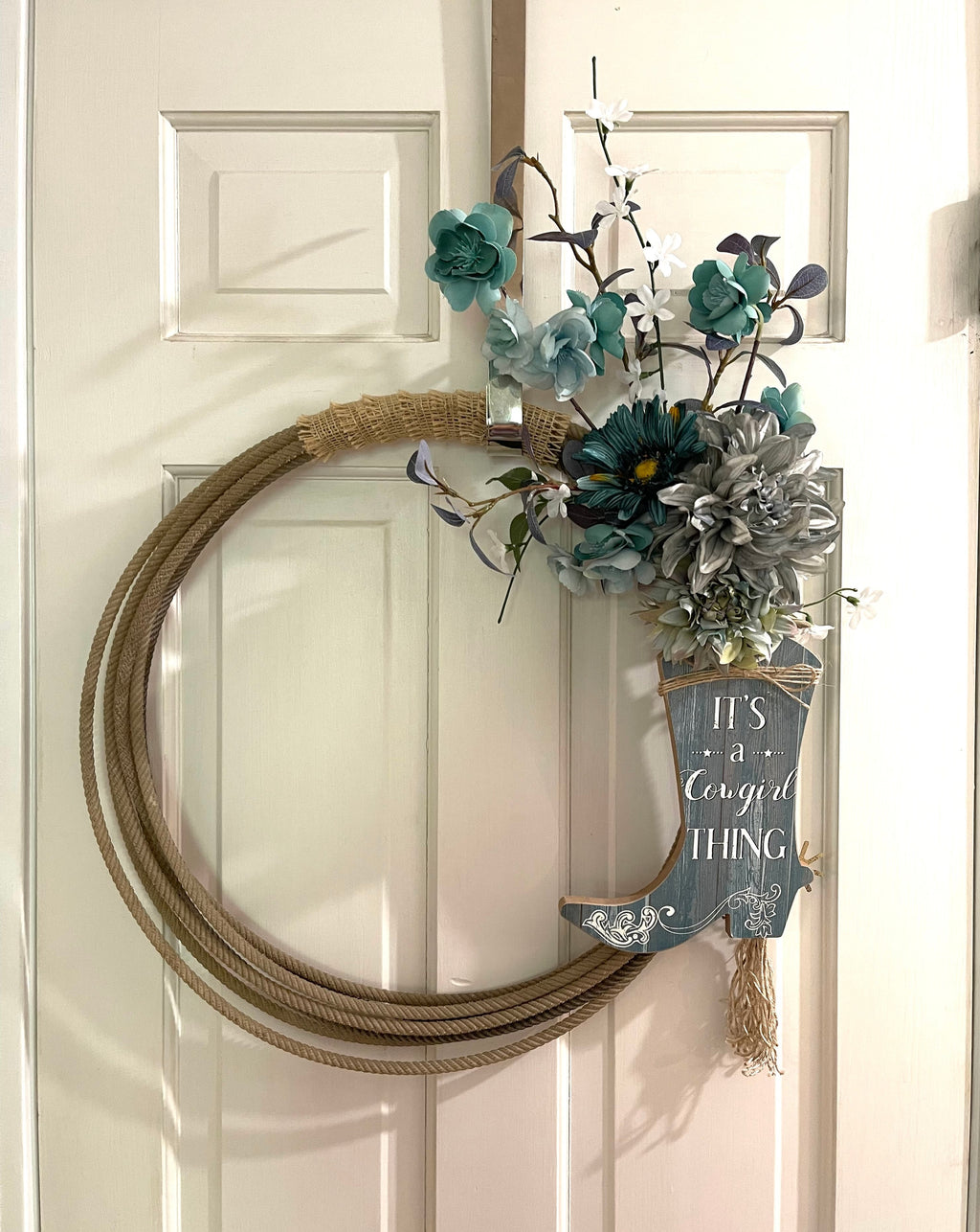 Handcrafted wreath on a upcycled lariat roping rope. Width: Approximately 22 inches. Florals and wood decor.