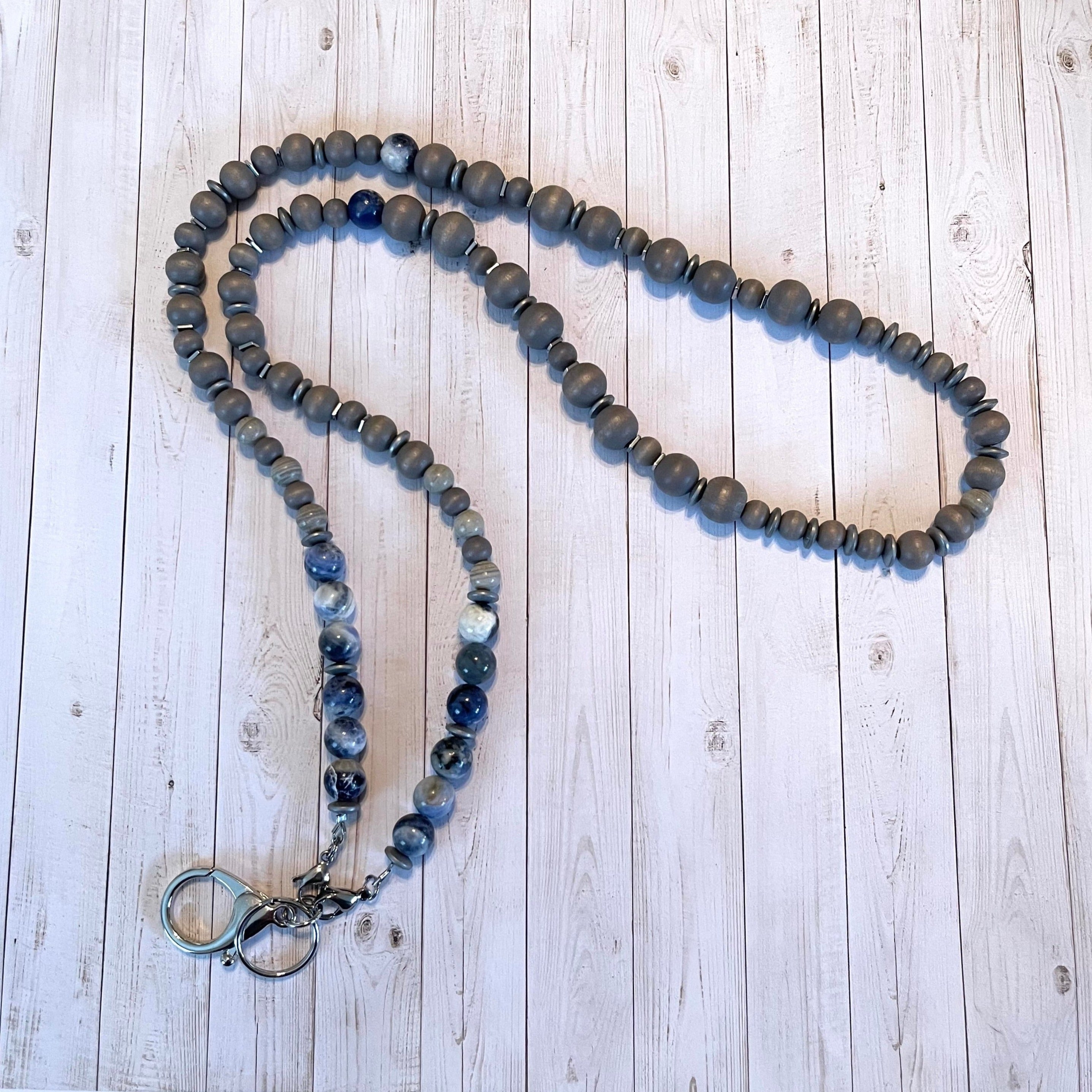 Handcrafted lanyard with stainless steel components and silver keyring and clasp. Beaded with wood beads, sodalite stones, gray agate stone, and hematite stones. 