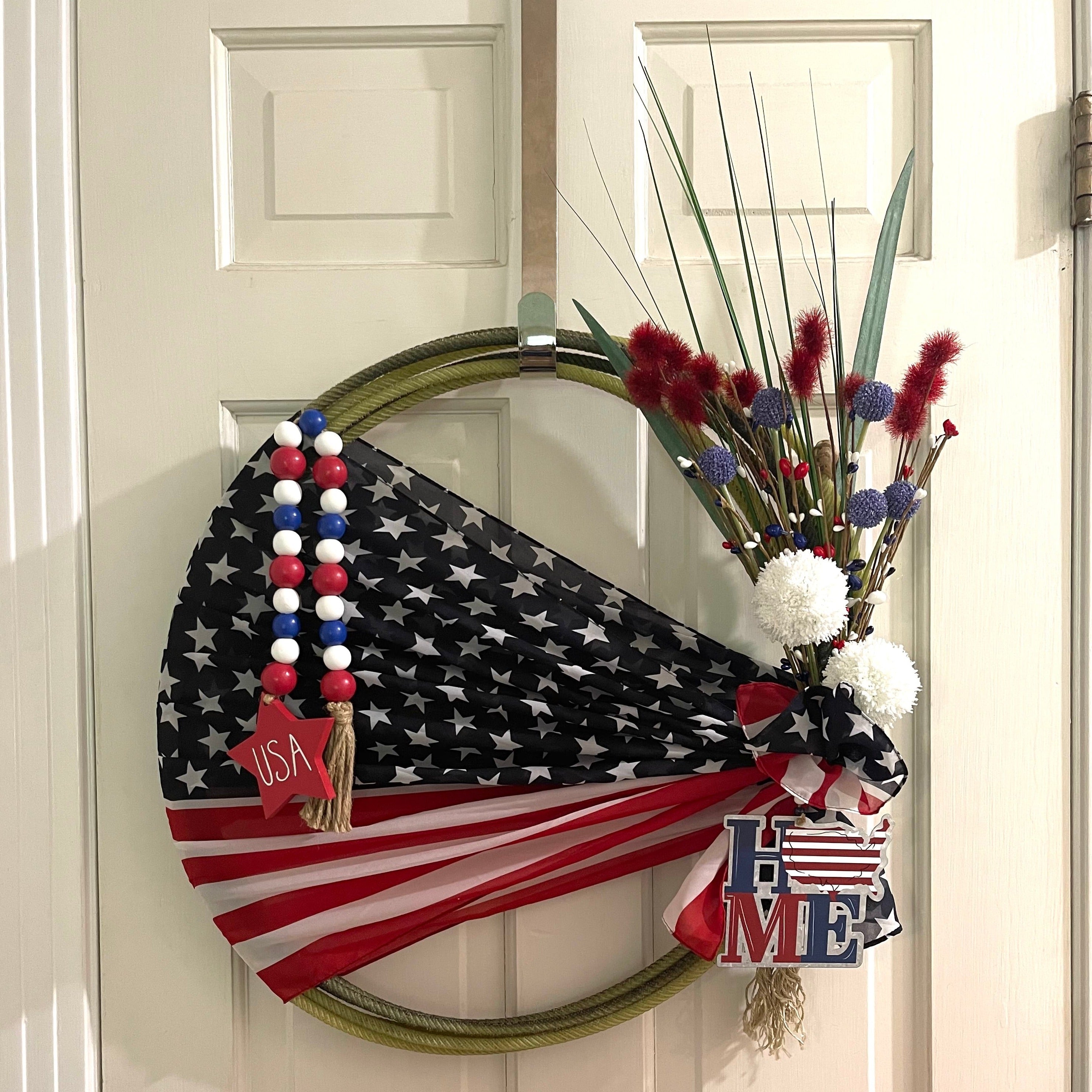 Handcrafted patriotic wreath on an upcycled lariat roping rope. Width: Approximately 20 inches. Florals and patriotic decorations.