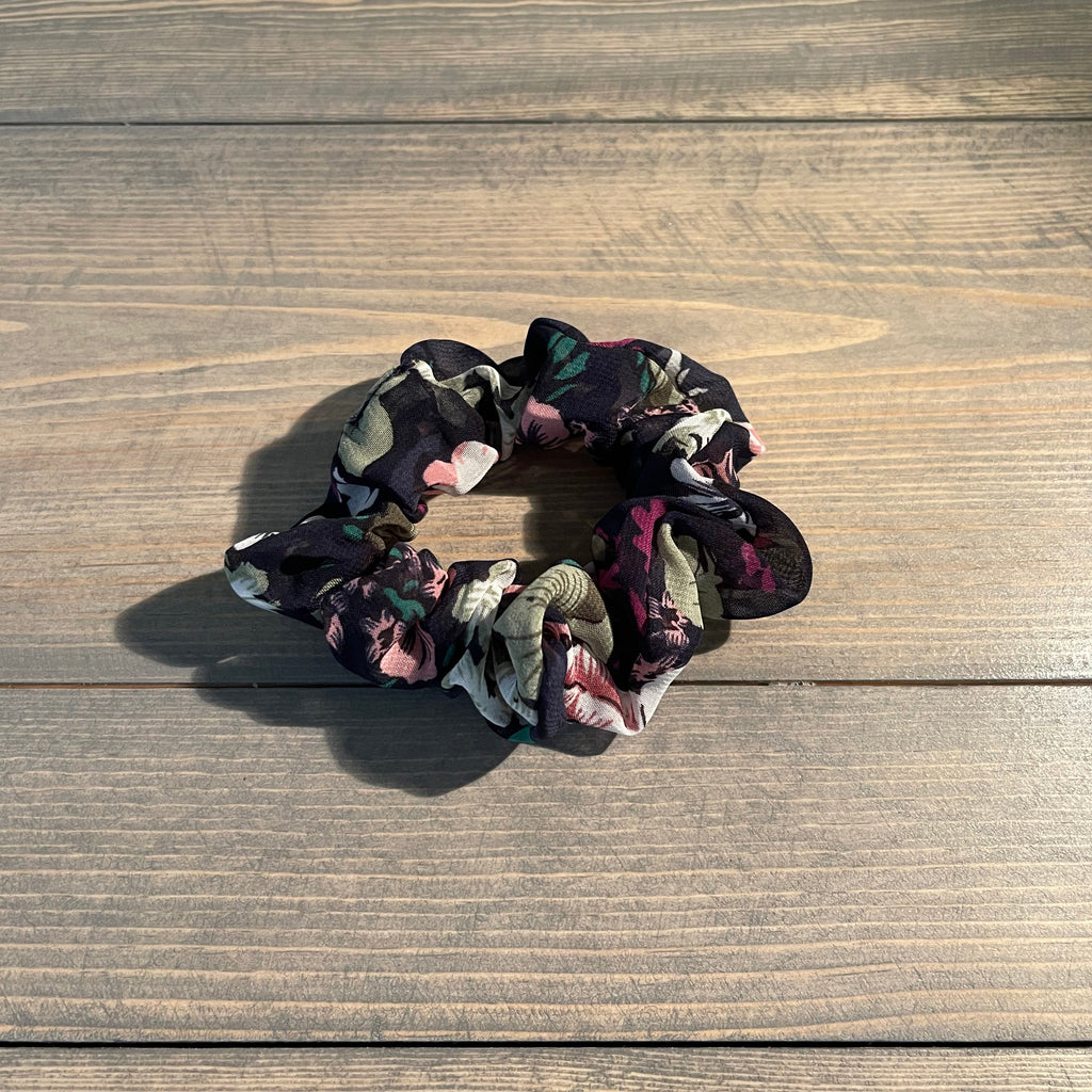 A sheer navy hair scrunchie with pink, purple, and green floral designs. 