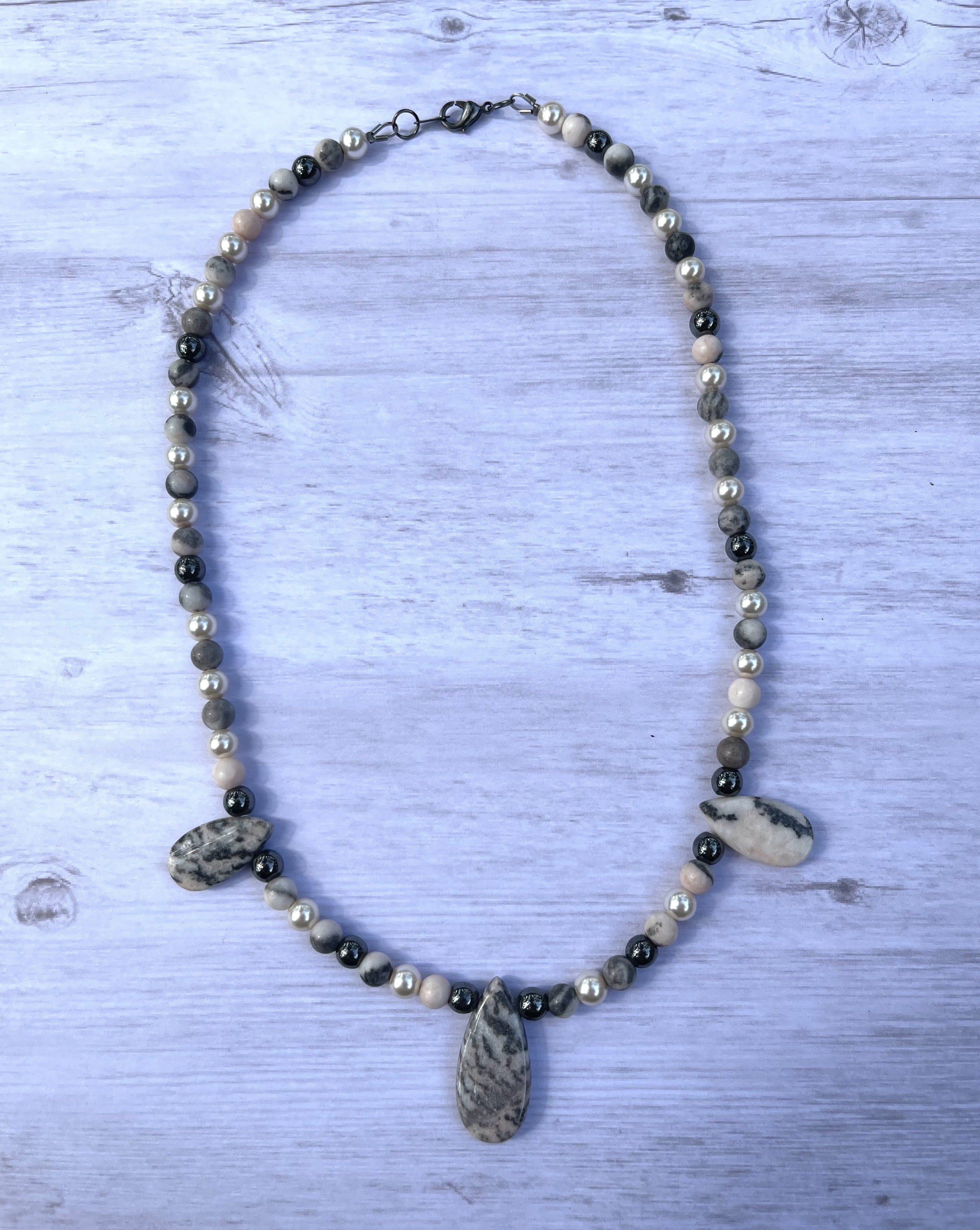 Handcrafted necklace with pink zebra jasper stones, black hematite stones, and glass pearl beads. Gunmetal clasp. Necklace length is approximately 17 inches.