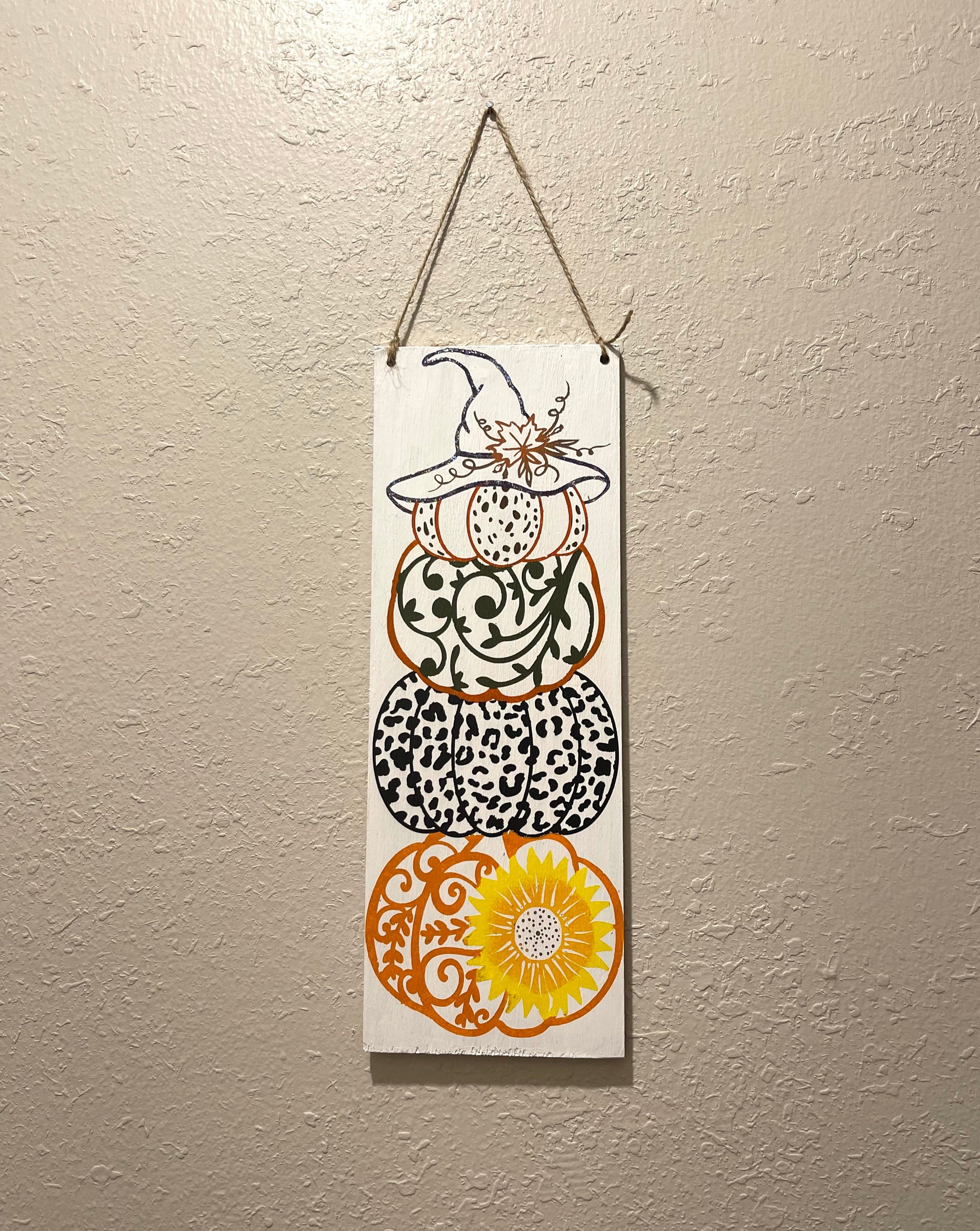 Wooden sign painted with a decorative stack of pumpkins. Hang on wall with twine. 12 1/2 inches tall and 4 1/2 inches wide. 