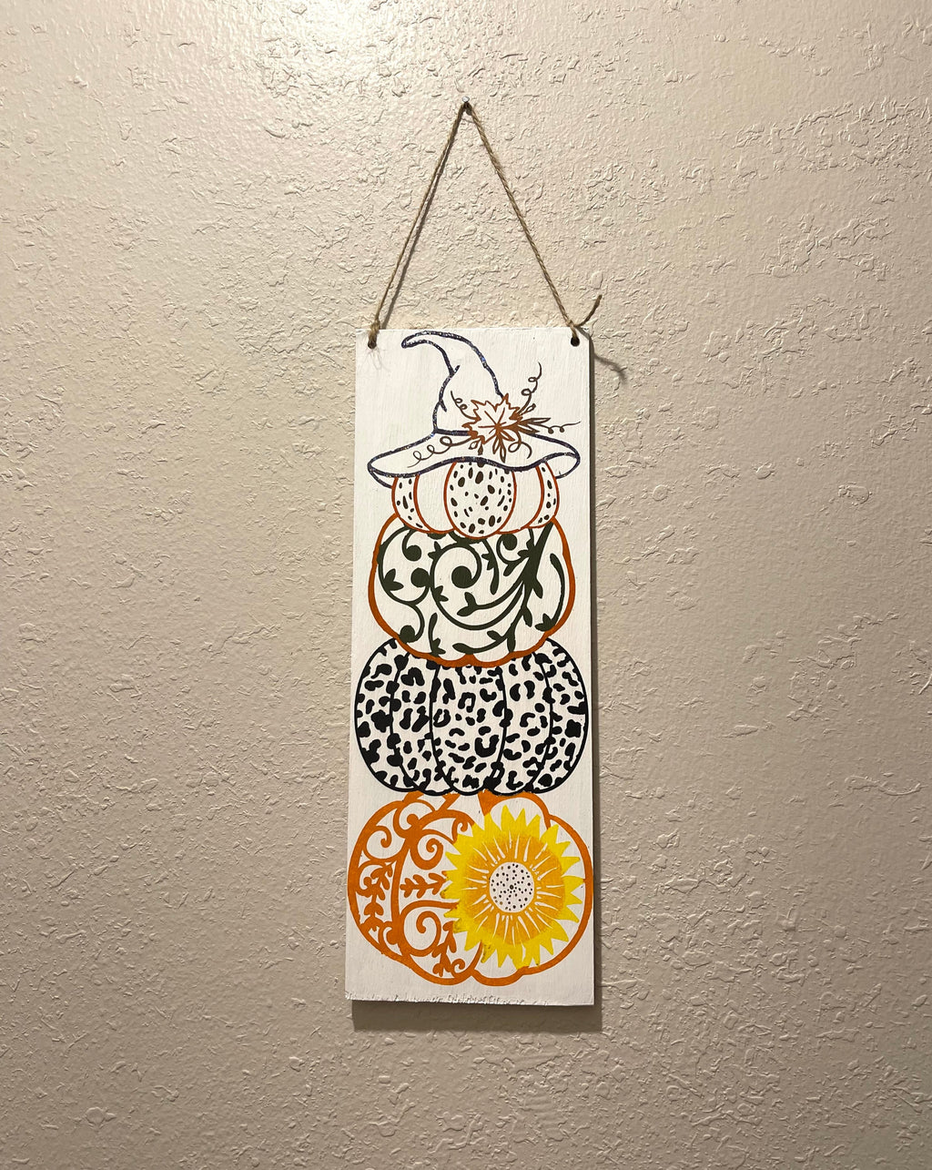 Wooden sign painted with a decorative stack of pumpkins. Hang on wall with twine. 12 1/2 inches tall and 4 1/2 inches wide. 