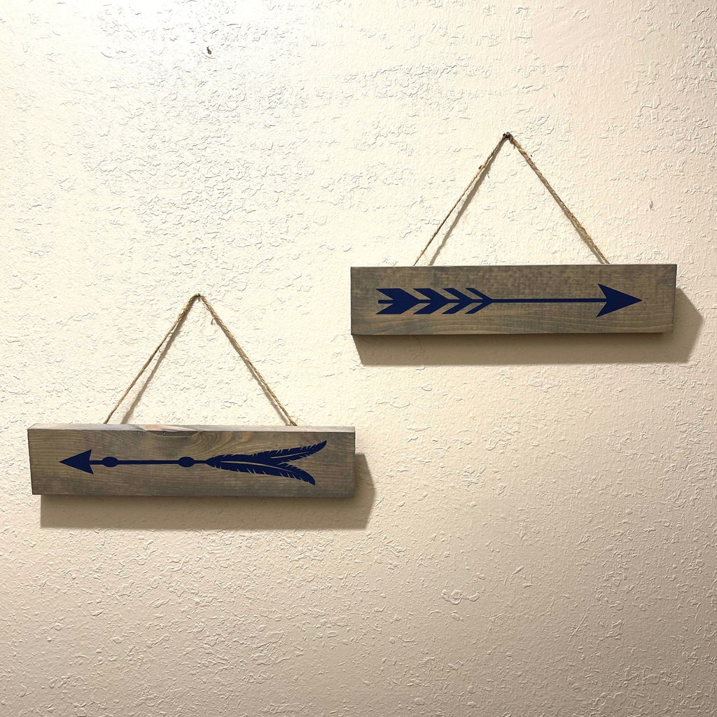 Set of 2 handcrafted wooden signs that hangs on the wall. Measures 11 1/2 x 2 1/2 inches. Wood is stained in a gray finish with blue arrows painted on them.