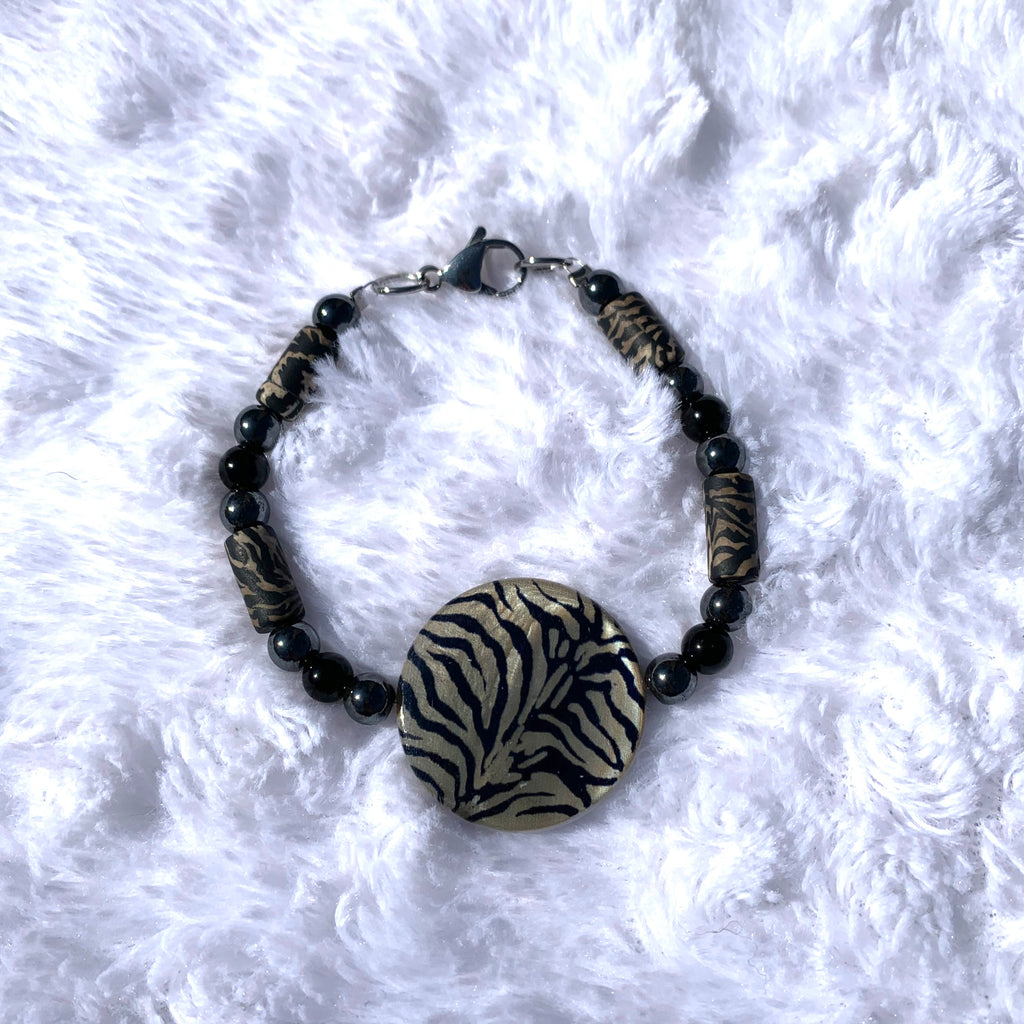 Handcrafted with a zebra shell disk, black glass beads, 6mm black hematite, and zebra clay cylinder beads. Bracelet has a stainless steel lobster clasp. Length is approximately 7 3/4 inches.