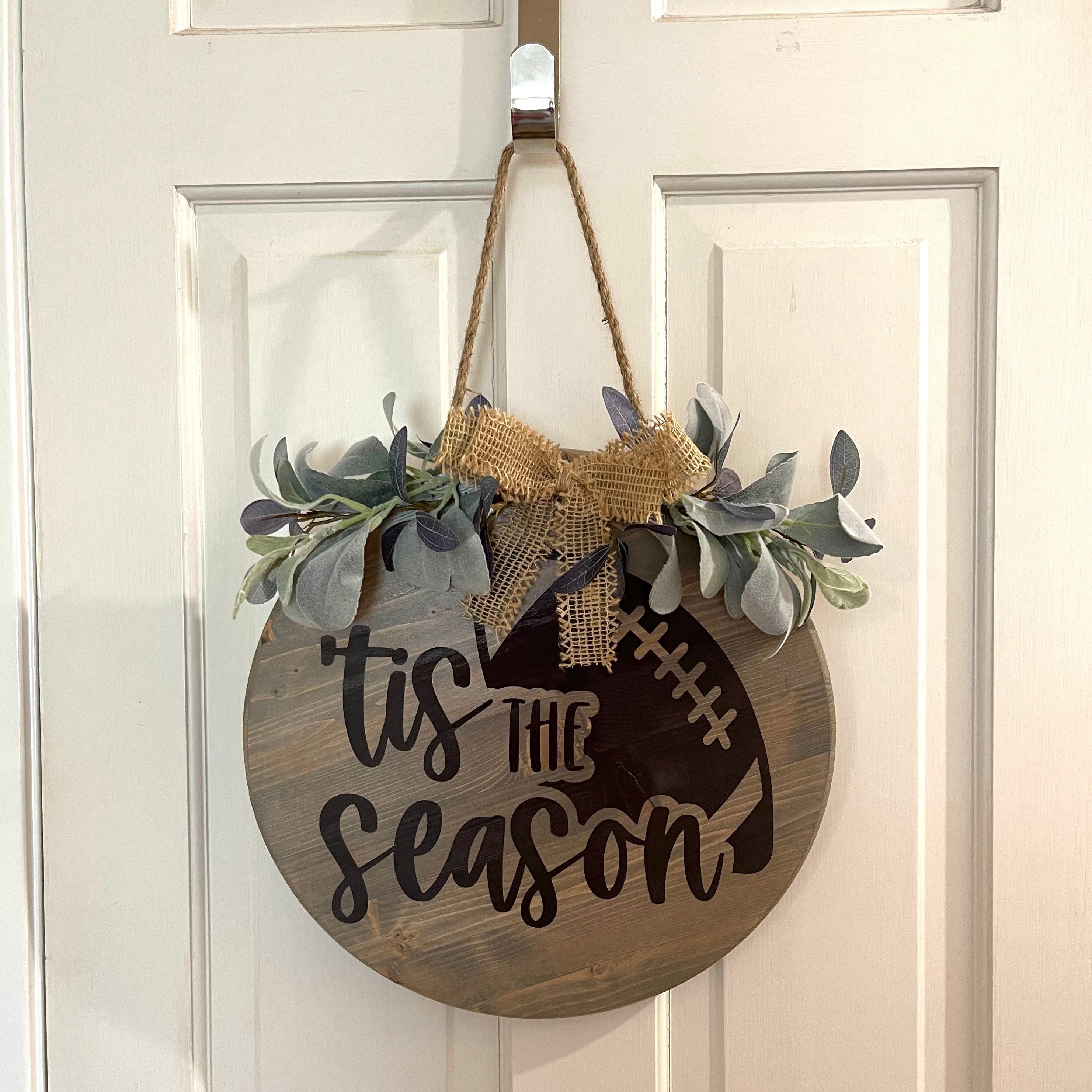 Handcrafted door hanger on a 15-in. x 15in. x 1-in . pine wood round board.  Tis the season for football painted design and stained.  Hangs on a jute cord.  Eucalyptus, lambs ear, and burlap.